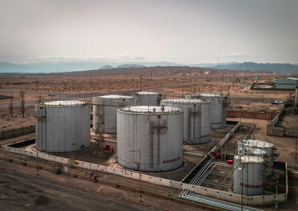 Aerial view of large industrial oil tanks in a desert setting with mountains in the distance.